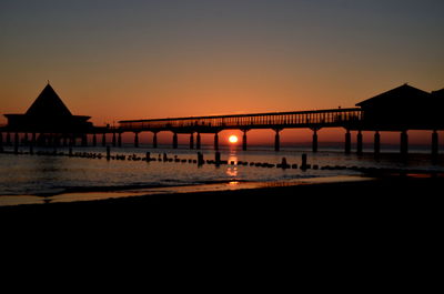 Silhouette pier over sea against orange sky