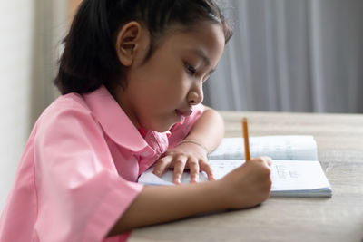 Side view of cute girl writing on paper at home