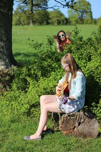 Girl sitting on field by tree playing a guitar