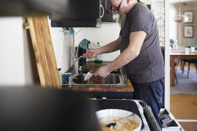 Man in kitchen washing dishes at kitchen sink