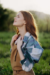 Young woman looking away while standing on field