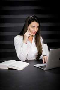 Young woman using mobile phone while sitting on table