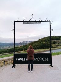 Rear view of woman standing by sign against sky