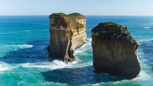 Rock formation in sea against clear blue sky