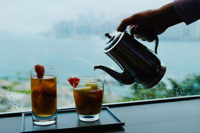 Cropped hand holding drink beside an ocean view window 