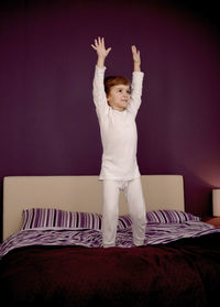 Low angle view of boy on bed against wall at home