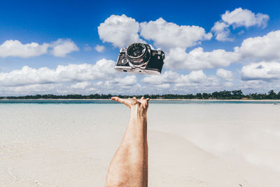 Cropped hand of man tossing camera at sandy beach