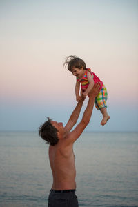 Full length of father and son on beach against sky