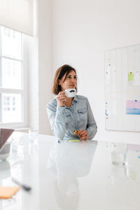 Portrait of woman holding smart phone while standing on laptop