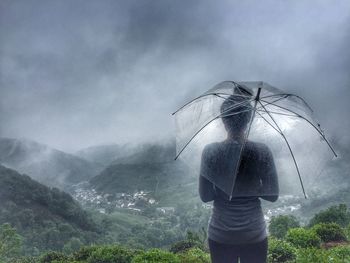 Rear view of woman with umbrella standing on mountain against cloudy sky