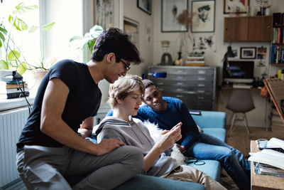 Friends looking at teenage boy using social media while studying in living room at home