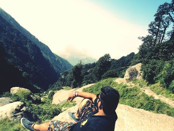 Man sitting on mountain against sky