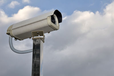 Low angle view of security camera against cloudy sky