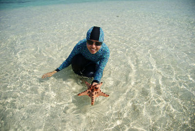 Portrait of smiling woman holding starfish at beach