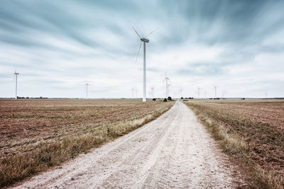 Country road passing through a field with wind turbines