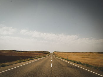 Empty road amidst field against sky