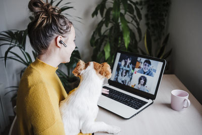 Woman talking with friends on video conference over digital tablet while sitting with pet at home