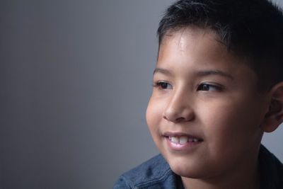 Close-up portrait of smiling boy against gray background