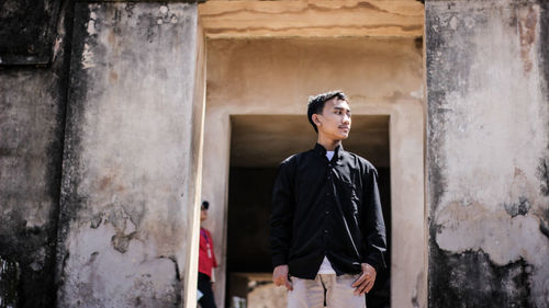 Young man looking away while standing against wall