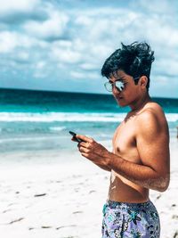 Shirtless young man using mobile phone at beach