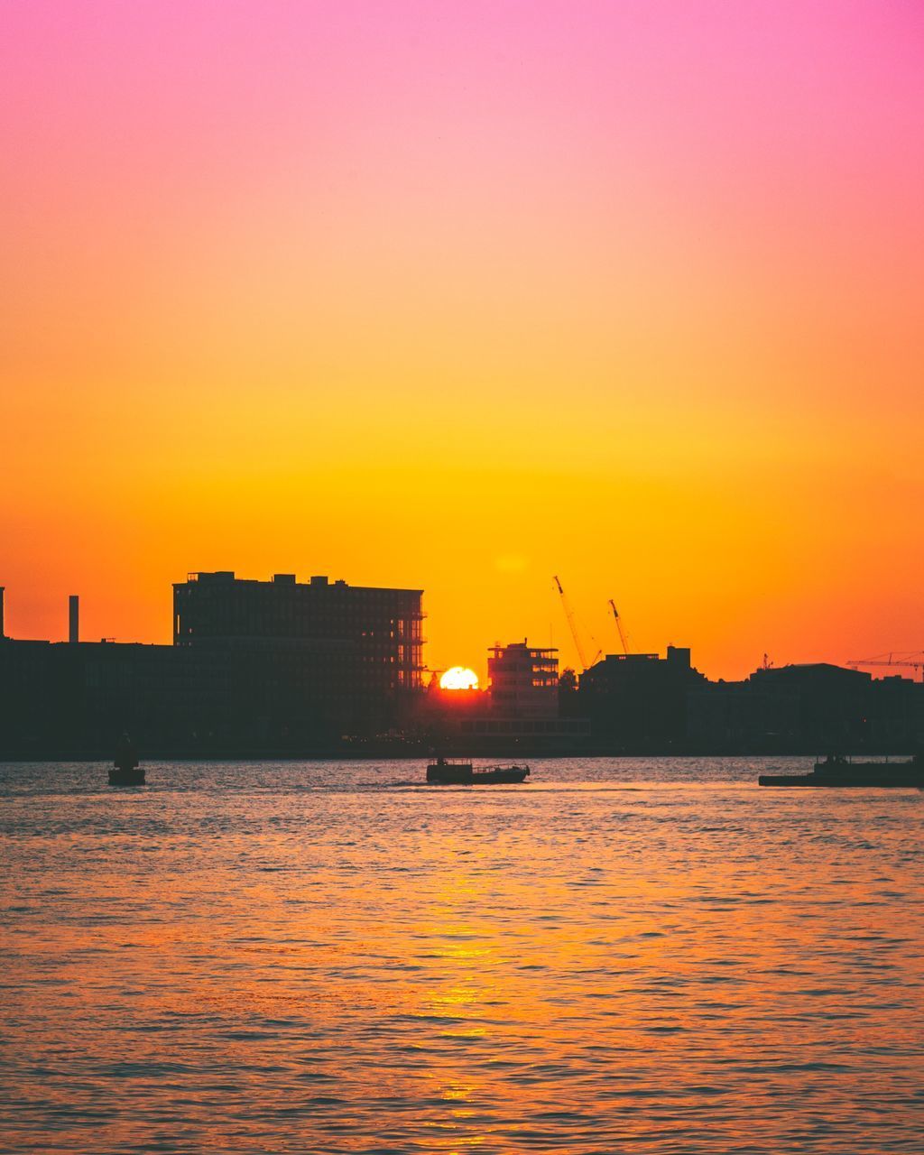 SILHOUETTE BUILDINGS BY SEA AGAINST ORANGE SKY