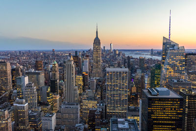 Empire state building amidst cityscape at manhattan during sunset