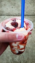 Cropped hand holding disposable glass with dessert