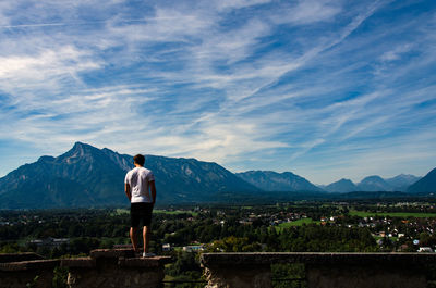 Rear view of man standing on retaining wall by landscape against sky