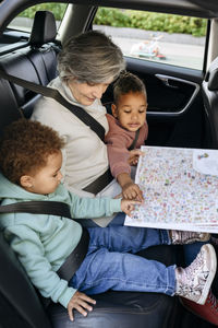 Senior woman reading book with children in car