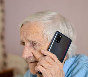 Happy elderly 90-year-old woman with glasses wearing a blue jacket smiles using a smartphone.