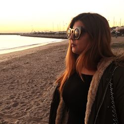 Thoughtful woman wearing sunglasses while standing at beach