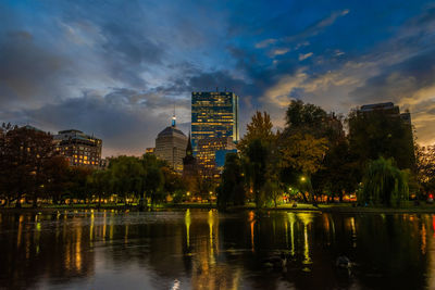 Illuminated buildings by river against sky at night