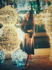 Portrait of smiling woman standing by illuminated decorations at night