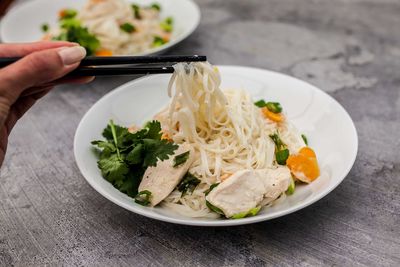 Close-up of hand having noodles in plate on table