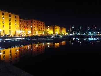 Illuminated buildings by river against sky at night