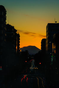 Traffic on street amidst silhouette buildings against sky during sunset