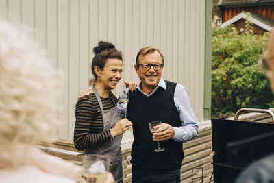 Smiling senior man and woman standing with arm around at back yard during garden party