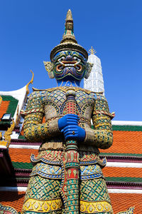 Low angle view of statue against temple building against clear blue sky