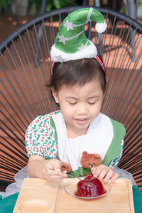 Happy charming 4 year old baby asian girl, preschooler child wear christmas tree hat eating jelly.