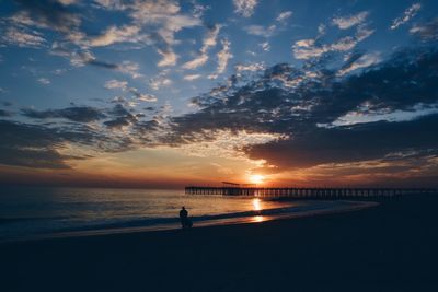 Silhouette people at beach against cloudy sky during sunset