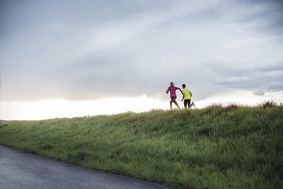 Rear view of determined athletes running on field against cloudy sky