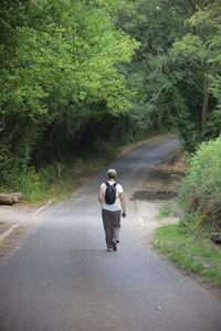 Rear view of woman walking on country road amidst trees