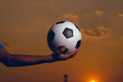 Low angle view of hand holding ball against sky during sunset