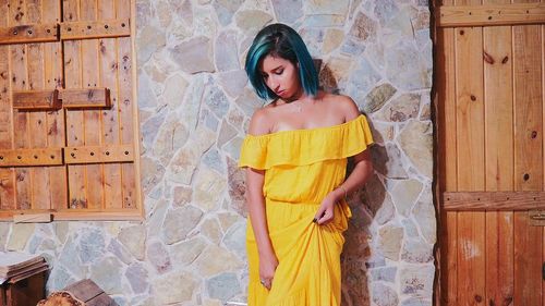 Young woman in yellow dress standing against wall