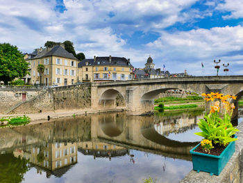 Arch bridge over river by buildings against sky