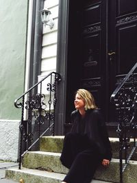 Smiling woman sitting on steps at house entrance