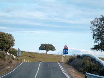 Road sign by trees against sky