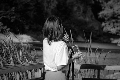 Rear view of woman sitting on railing against plants