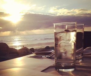 Close-up of beer on table against sea during sunset