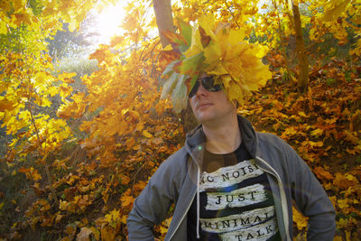 Man with leaves on head standing at forest during autumn